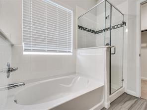 Oval soaking tub, separate glass-enclosed shower, polished chrome fixtures, white tile surround, and wood-finish flooring