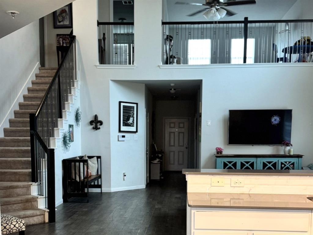 Two-story living area with high ceilings, staircase featuring black iron balusters, wood-finish flooring, and an open-concept layout