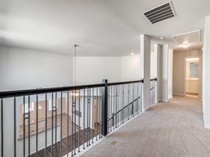 Upper level gallery featuring metal balusters with a dark handrail, neutral carpeting, and a recessed ceiling design