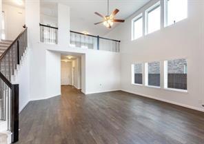 Expansive two-story room featuring vaulted ceilings, wood-finish flooring, large windows, a ceiling fan, and a metal-railed staircase