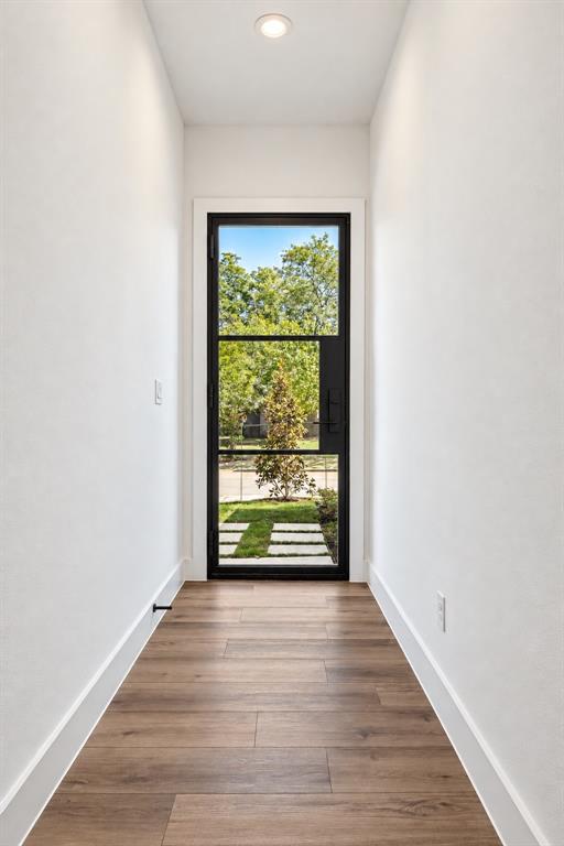 Black-framed glass entry door with wood-finish flooring and recessed ceiling lighting