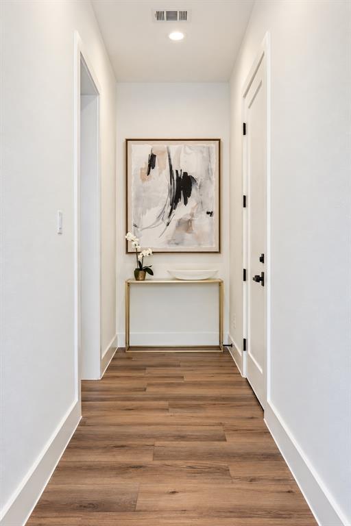 Recessed ceiling lighting, wood-finish flooring, white walls, white trim, and a white door with black hardware