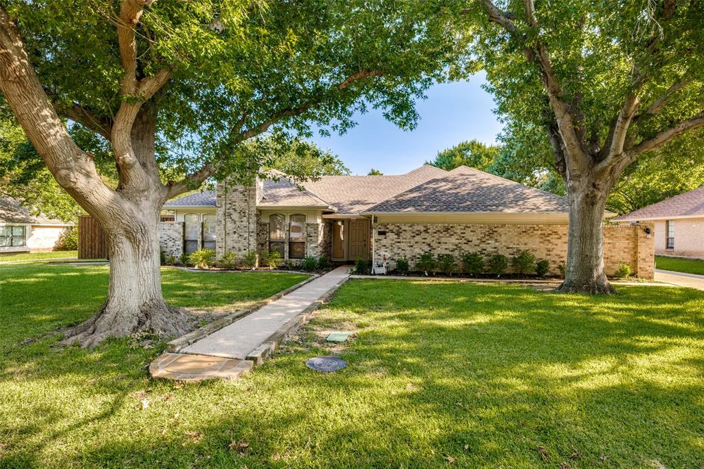 Single-story brick exterior featuring a multi-gabled roofline, concrete walkway, and expansive front lawn with mature trees