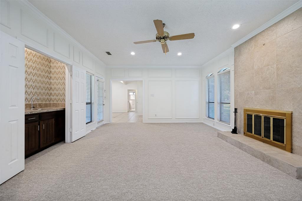 Living area featuring floor-to-ceiling stone fireplace surround, custom wall paneling, built-in wet bar with cabinetry, and recessed lighting
