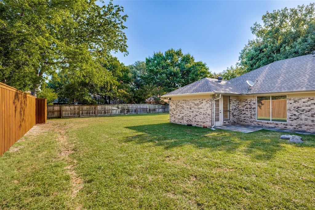Expansive backyard featuring a full-perimeter wood privacy fence, brick exterior siding, and mature trees