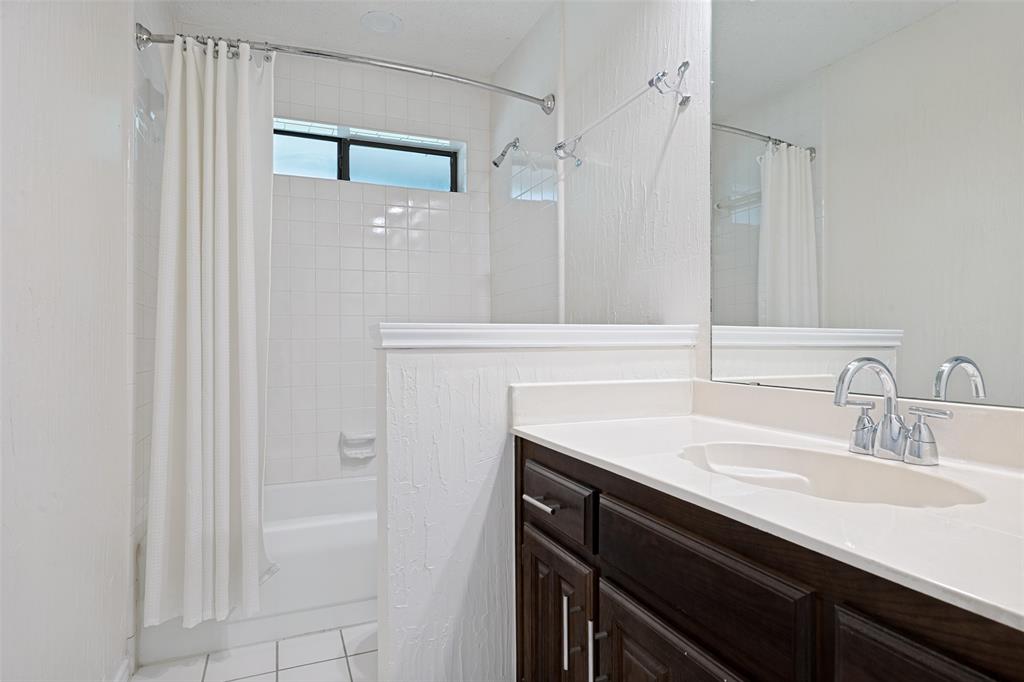 Dark wood-finish vanity with a white countertop, integrated sink, polished chrome faucet, and a wall-to-wall mirror