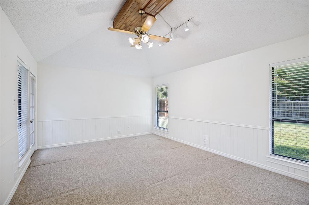Vaulted ceiling featuring a wood-beam accent, beadboard wainscoting, carpeted flooring, track lighting, and multiple windows with horizontal blinds