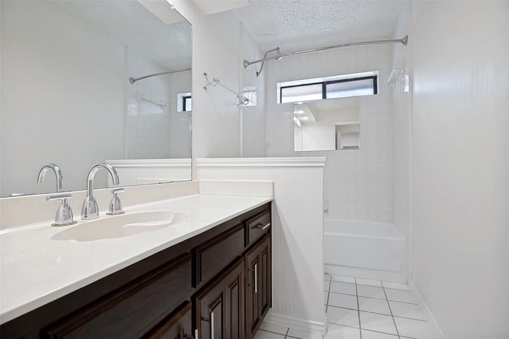 Bathroom featuring dark-stained cabinetry, a white countertop with an integrated basin, a polished chrome dual-handle faucet, a full-width mirror, and a tile-surround bathtub
