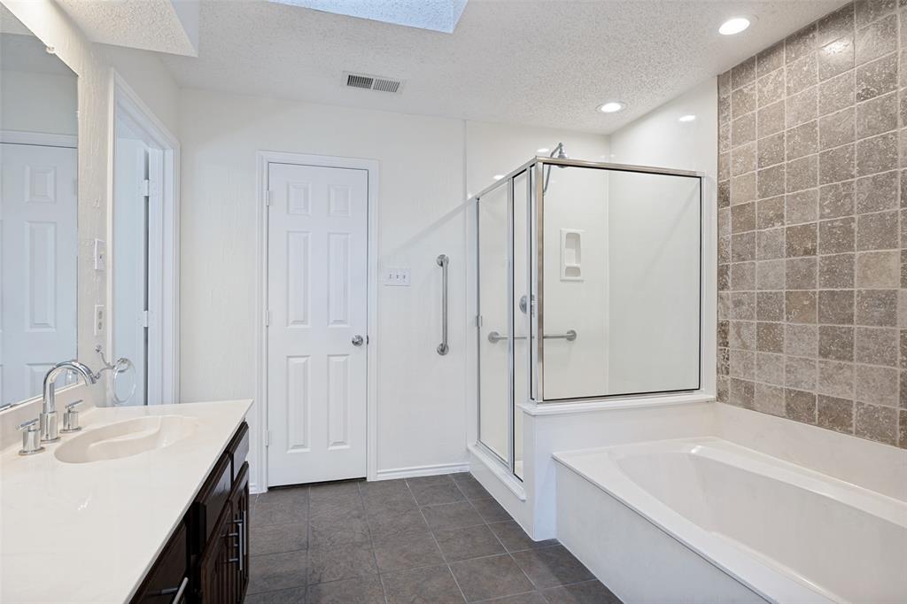 Bathroom featuring a dark wood-finish vanity with a light-toned countertop, a glass-enclosed shower, a deep soaking tub with a tiled accent wall, and recessed lighting