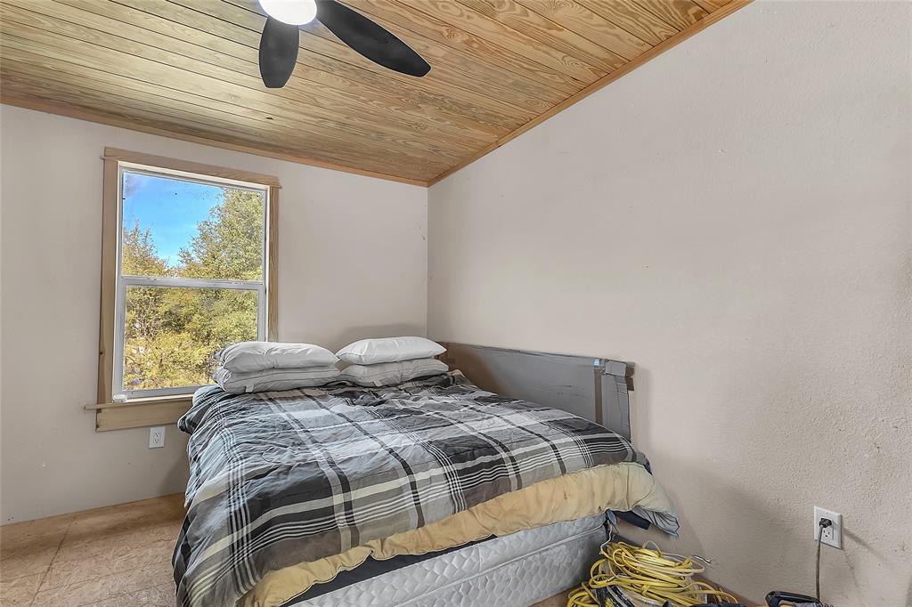 Bedroom with wood plank ceiling, ceiling fan, and tree view window