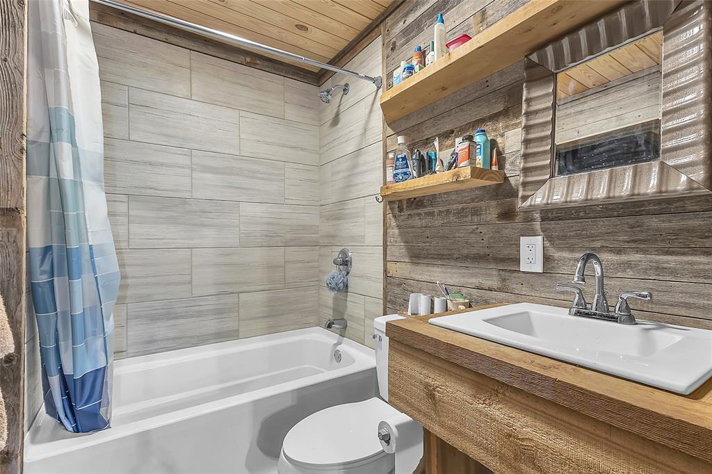 Bathroom with tub-shower, wood-plank walls, and wood vanity