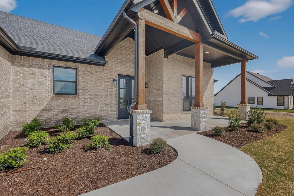 Exterior featuring light-toned brick facade, timber-framed gabled entryway with stone-based pillars, concrete walkway, and dark-finished window trim