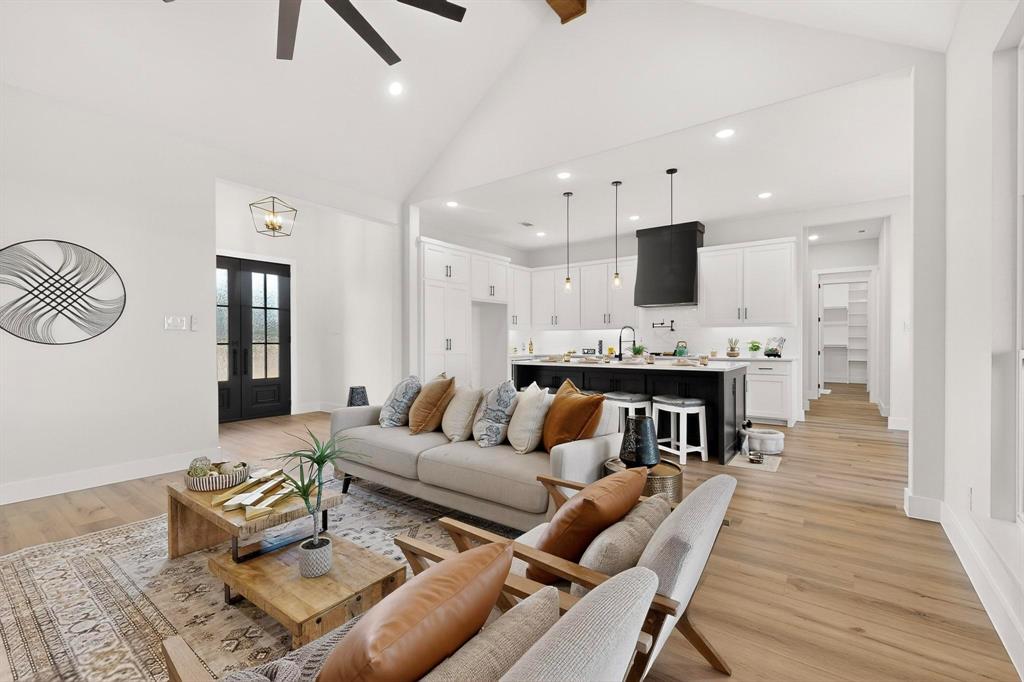 Open-concept space featuring vaulted ceilings, wood-finish flooring, a kitchen island with contrasting cabinetry, recessed lighting, and black double-entry doors