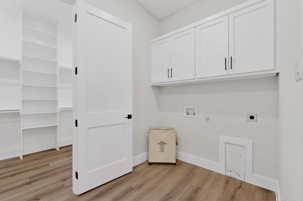 Laundry area featuring wood-finish flooring, white shaker-style cabinetry with matte black pulls, built-in shelving, and a two-panel interior door with matte black hardware