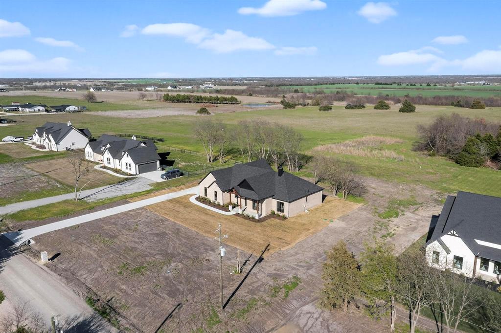 Single-story residence featuring a multi-gabled roofline, light-toned masonry exterior, concrete driveway, and expansive rear acreage