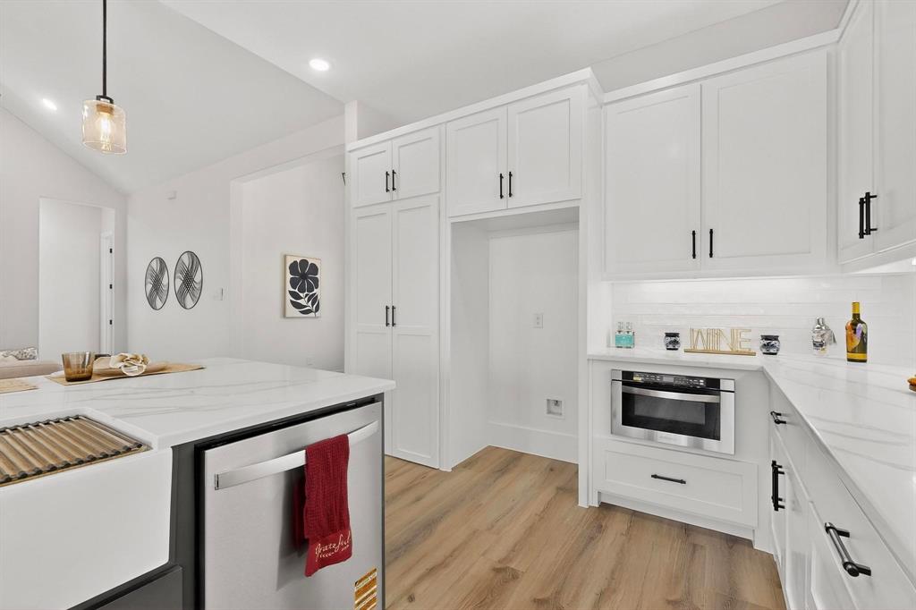 Kitchen featuring white shaker-style cabinetry, matte black hardware, stone-finish countertops, wood-finish flooring, and a built-in microwave