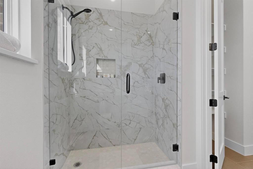 Walk-in shower featuring floor-to-ceiling stone-finish tile, a frameless glass door, recessed wall niche, and matte black hardware