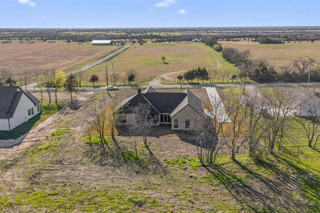 Single-story residence with a masonry exterior, high-pitched roof, concrete driveway, and expansive acreage featuring mature trees