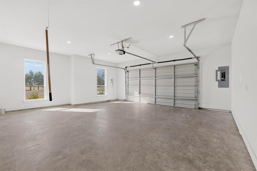 Spacious garage featuring finished walls, recessed lighting, concrete flooring, dual windows, and an automated overhead door system
