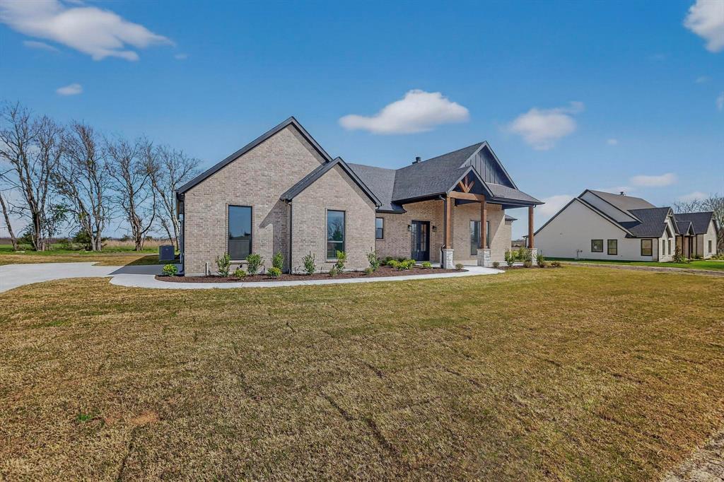 Brick exterior featuring a multi-gabled roofline, covered entryway with wood-beam detailing, stone column bases, and concrete driveway