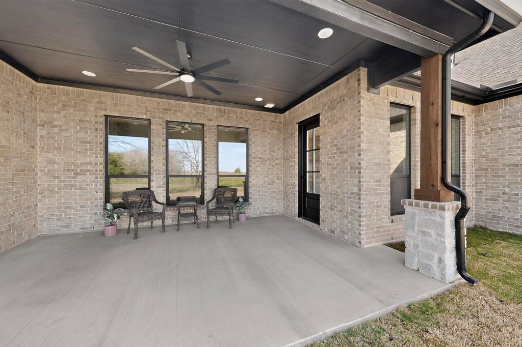 Covered patio featuring a concrete floor, light-colored brick exterior walls, a dark-finished ceiling with recessed lighting, a modern ceiling fan, and a timber-wrapped column on a stone base