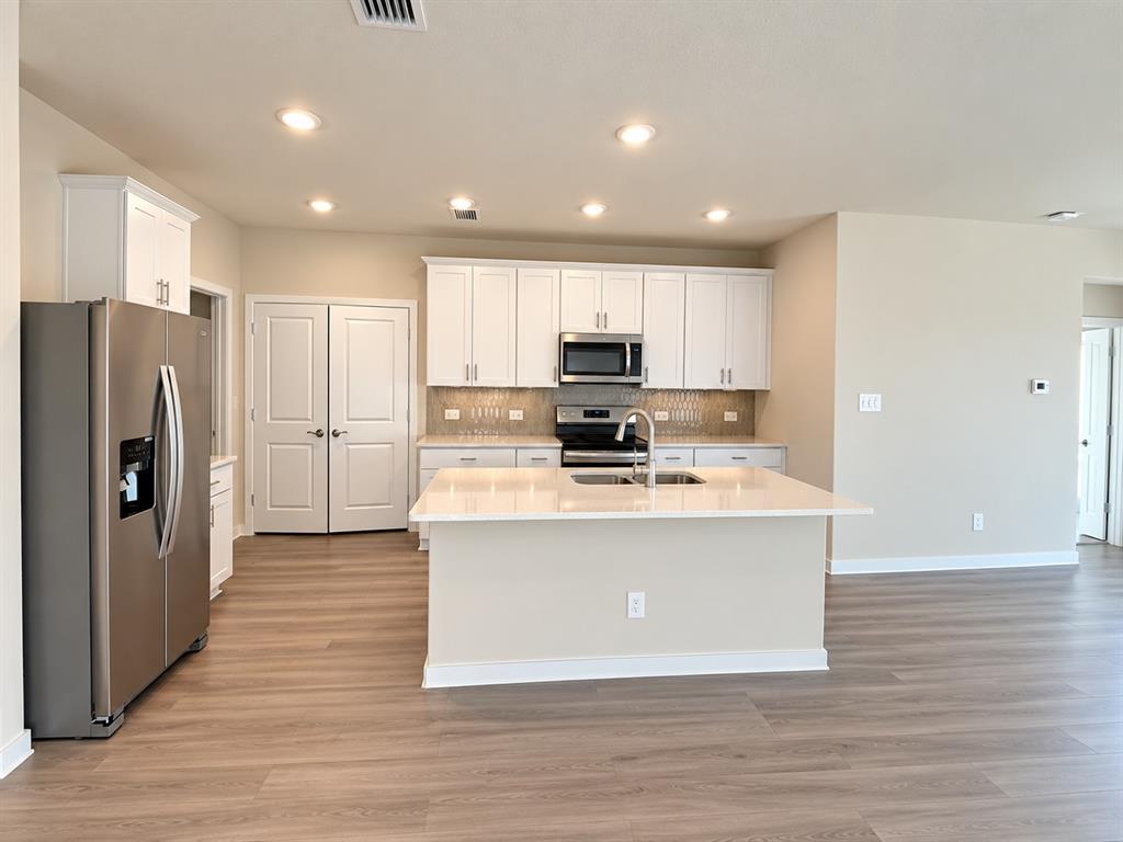 Kitchen featuring white cabinetry, quartz countertops, a central island with a double-basin sink, stainless steel appliances, and wood-finish flooring