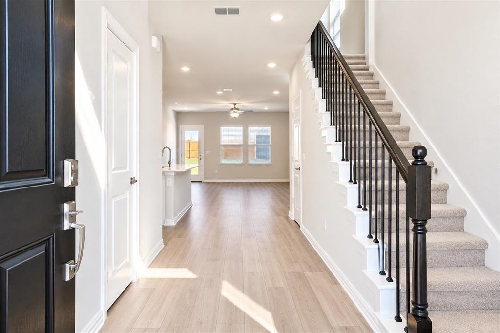 Wood-finish flooring, recessed lighting, carpeted staircase with dark wood newel post and black metal balusters, and a kitchen island with a single-basin sink
