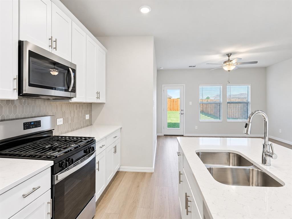 Kitchen featuring white cabinetry, stainless steel appliances, a double basin sink, and light-toned wood-finish flooring