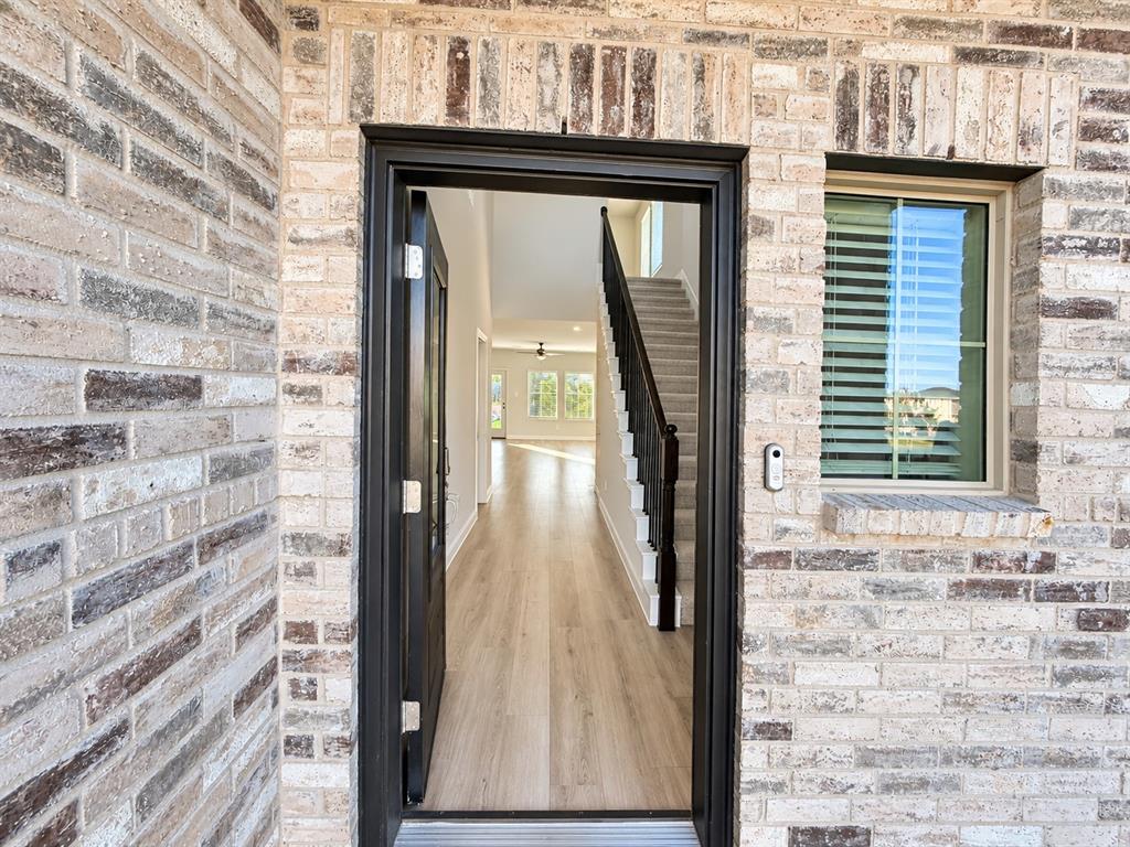 Textured brick facade with a dark-framed entryway, wood-finish flooring, and a staircase featuring a dark stained handrail and balusters