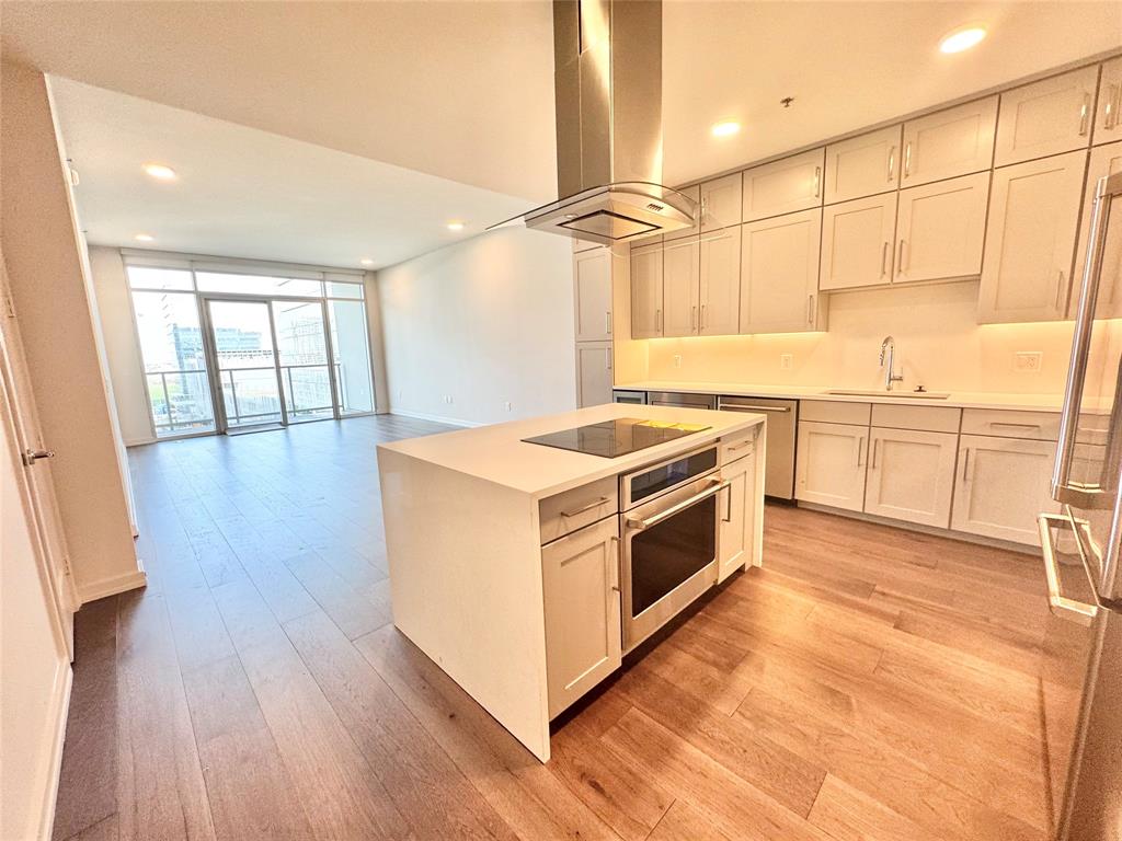 Kitchen with appliances with stainless steel finishes, sink, expansive windows, island exhaust hood, and light hardwood / wood-style floors