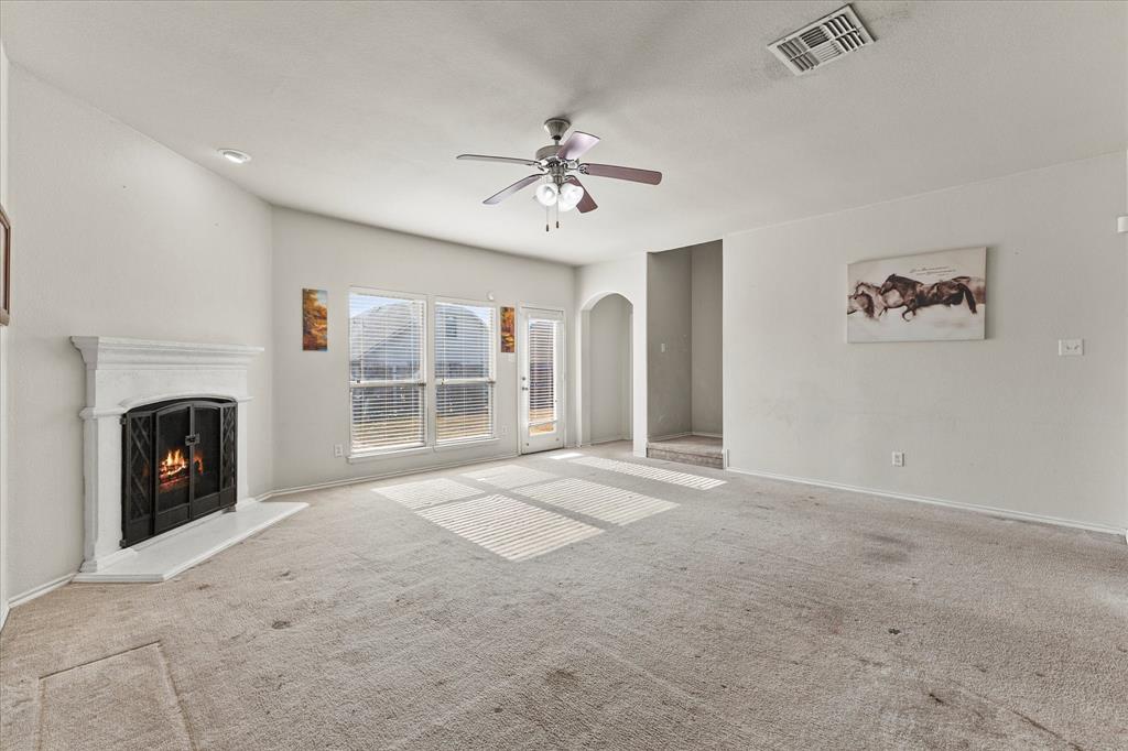 Living area featuring a fireplace with a white mantel, ceiling fan with integrated lighting, dual windows, and an arched entry