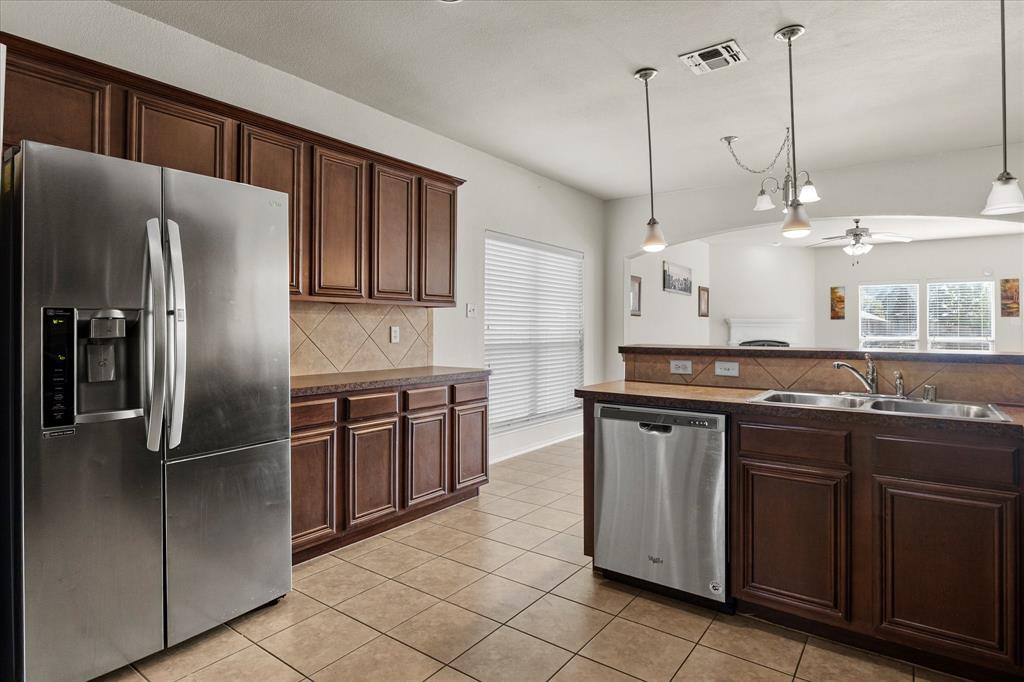 Kitchen featuring dark wood cabinetry, stainless steel appliances, tile backsplash, laminate countertops, and pendant lighting Kitchen featuring dark wood cabinetry, stainless steel appliances, tile backsplash, laminate countertops, and pendant lighting