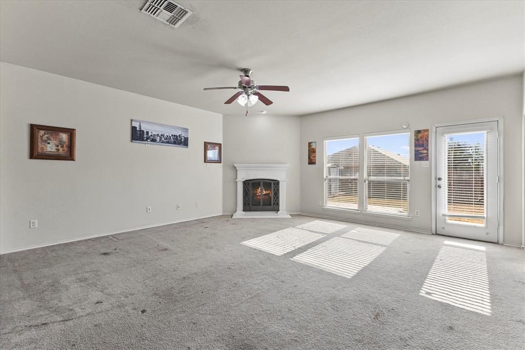 Corner fireplace with a white mantel, ceiling fan with light fixture, large windows, and a glass-paneled exterior door