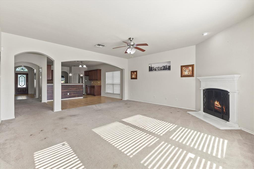 Living area featuring an arched entryway, recessed ceiling, fireplace with a white mantel, ceiling fan, and carpeted flooring