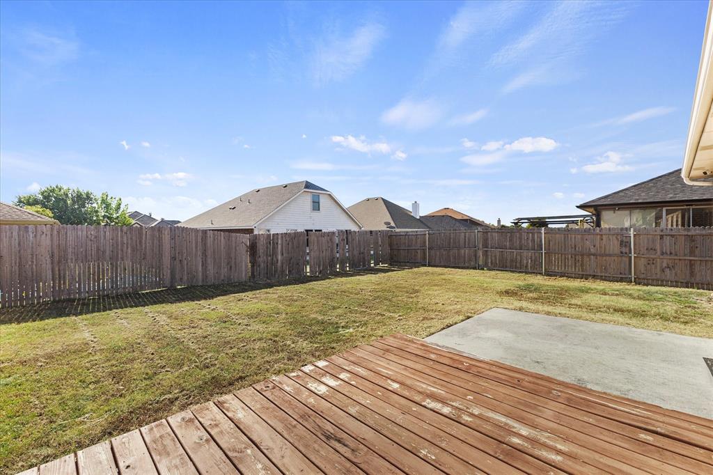 Rear exterior featuring a wood-plank deck, concrete patio, and fenced yard