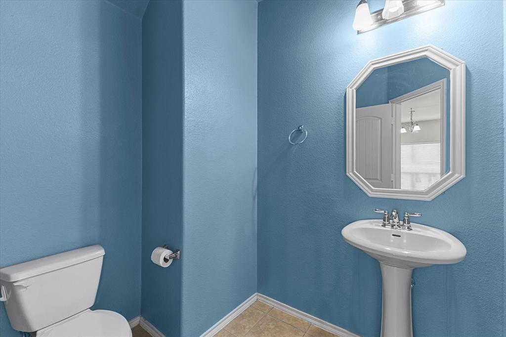 Powder room featuring a pedestal sink, wall-mounted light fixture, octagonal wall mirror, and tile flooring