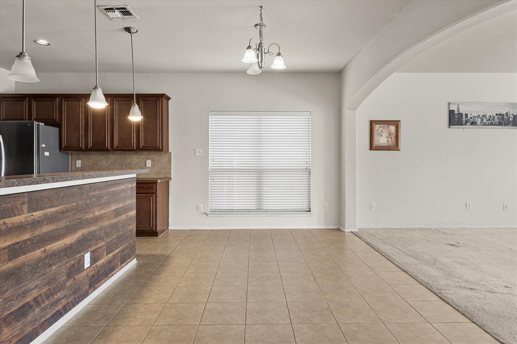 Kitchen featuring dark wood cabinetry, a breakfast bar with a wood-plank finish, tiled flooring, three pendant lights, and a central chandelier