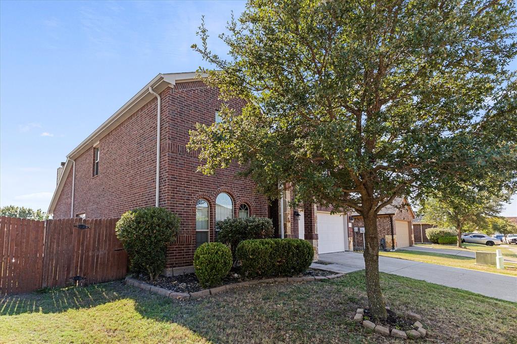 Two-story brick exterior featuring arched windows, a front-facing attached garage, and landscaped garden beds with mature trees Two-story brick exterior featuring arched windows, a front-facing attached garage, and landscaped garden beds with mature trees
