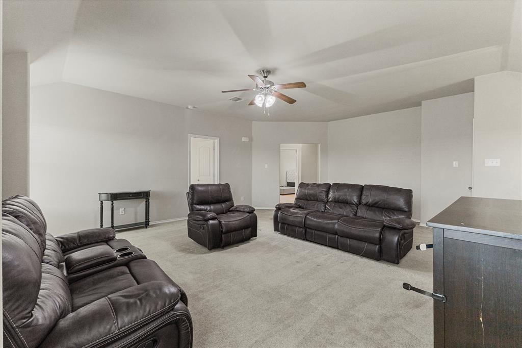Vaulted ceiling, neutral wall tones, carpeted flooring, and a central ceiling fan with integrated lighting