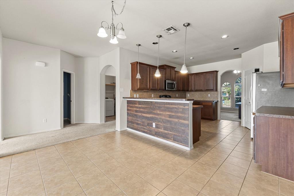 Kitchen featuring wood cabinetry, a breakfast bar with wood-plank surfacing, pendant lighting, tile flooring, and arched doorways