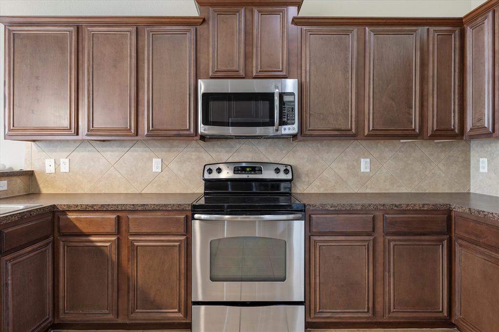 Kitchen featuring wood cabinetry with crown molding, stainless steel microwave, stainless steel range, and diagonal tile backsplash Kitchen featuring wood cabinetry with crown molding, stainless steel microwave, stainless steel range, and diagonal tile backsplash
