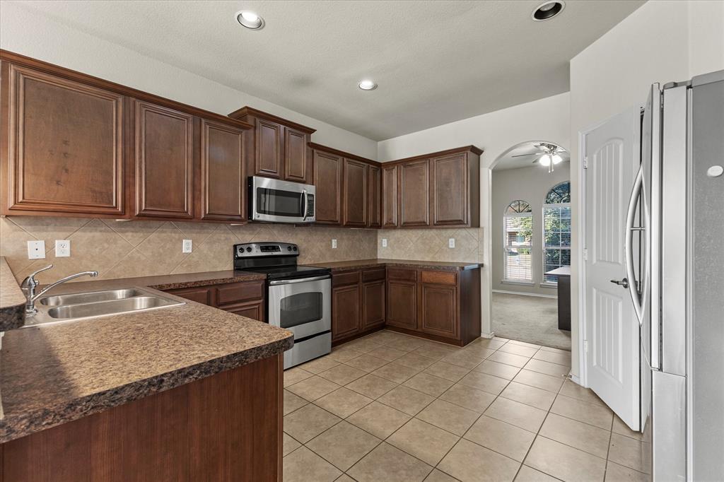 Kitchen featuring dark-finish wood cabinetry, stainless steel appliances, tiled backsplash, ceramic floor tiling, and recessed lighting Kitchen featuring dark-finish wood cabinetry, stainless steel appliances, tiled backsplash, ceramic floor tiling, and recessed lighting