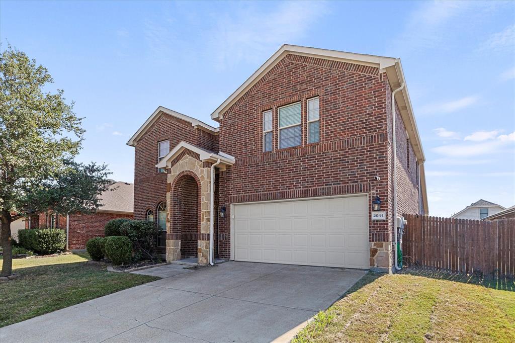 Two-story brick exterior featuring a stone-trimmed arched entryway, multi-paned windows, a two-car garage, and a wood privacy fence Two-story brick exterior featuring a stone-trimmed arched entryway, multi-paned windows, a two-car garage, and a wood privacy fence