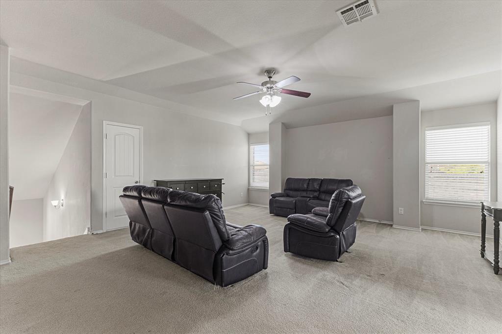 Vaulted ceilings featuring a central ceiling fan with integrated lighting, neutral wall tones, carpeted flooring, and oversized windows with horizontal blinds
