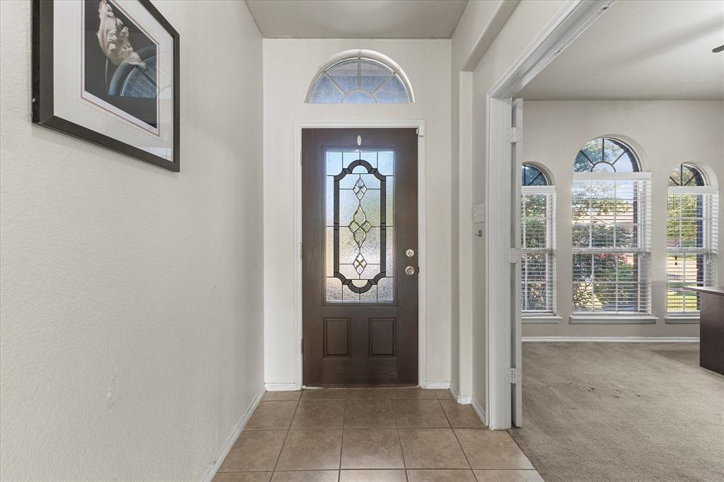 Entryway featuring a dark wood door with decorative glass inlay, an arched transom window, and neutral tile flooring Entryway featuring a dark wood door with decorative glass inlay, an arched transom window, and neutral tile flooring
