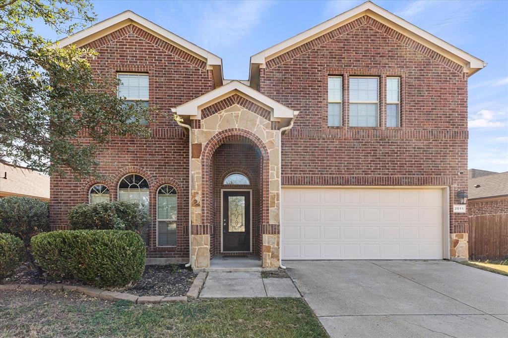 Two-story brick exterior featuring a stone-trimmed arched entryway, multi-pane windows, and an attached two-car garage Two-story brick exterior featuring a stone-trimmed arched entryway, multi-pane windows, and an attached two-car garage