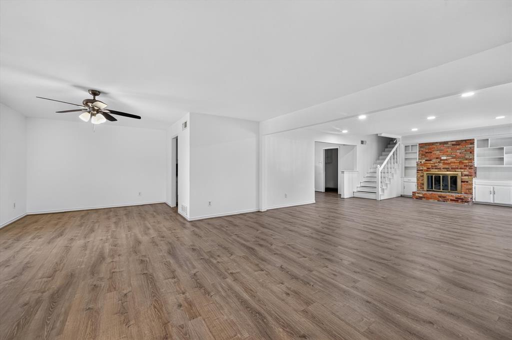 Open-concept living space featuring wood-finish flooring, recessed lighting, a ceiling fan, a floor-to-ceiling brick fireplace, and built-in shelving Open-concept living space featuring wood-finish flooring, recessed lighting, a ceiling fan, a floor-to-ceiling brick fireplace, and built-in shelving