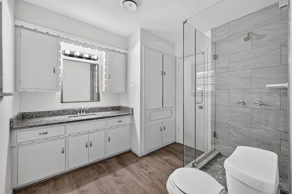 Bathroom featuring a white vanity with stone-finish countertop, wood-finish flooring, full-height built-in cabinetry, and a walk-in shower with a glass enclosure and tile surround