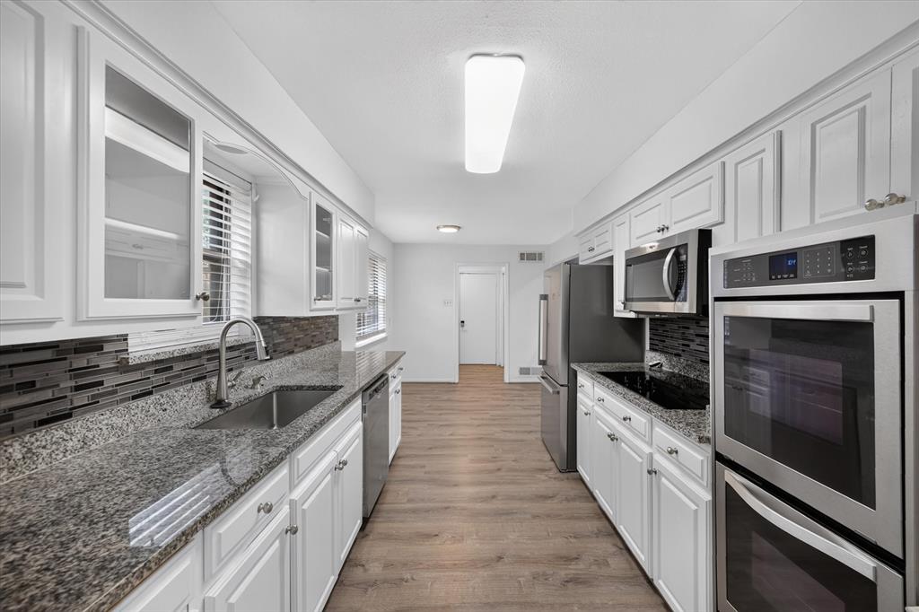Kitchen featuring white shaker-style cabinetry, stone countertops, stacked-tile backsplash, wood-finish flooring, and stainless steel double wall ovens Kitchen featuring white shaker-style cabinetry, stone countertops, stacked-tile backsplash, wood-finish flooring, and stainless steel double wall ovens