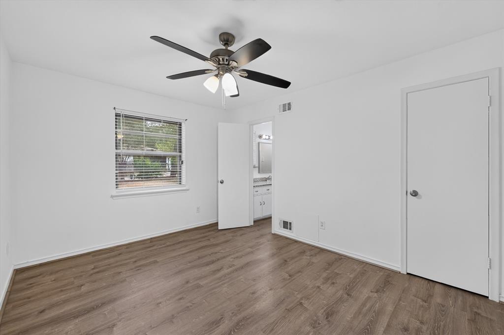 Neutral-toned room featuring wood-finish flooring, a multi-blade ceiling fan with integrated lighting, and a window with horizontal blinds